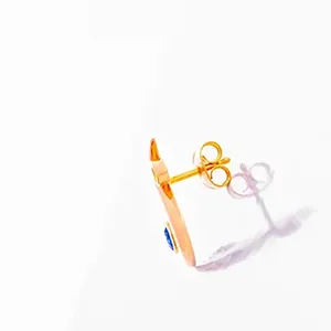 Minimalistische Schmuckfotografie – Goldohrring kunstvoll inszeniert von Michael Schalansky Professionelle Produktfotografie eines einzelnen goldenen Ohrsteckers in seitlicher Ansicht. Man sieht den Stift des Ohrrings und den Butterfly-Verschluss (Ohrstopper), sowie einen kleinen blauen Stein an der Vorderseite des Ohrrings. Das Schmuckstück liegt auf einer reflektierenden Plexiglasoberfläche, die eine klare Spiegelung zeigt.